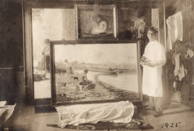 Pedro Bruno no ateliê ao lado de uma pintura, em fotografia identificada com o ano de 1925